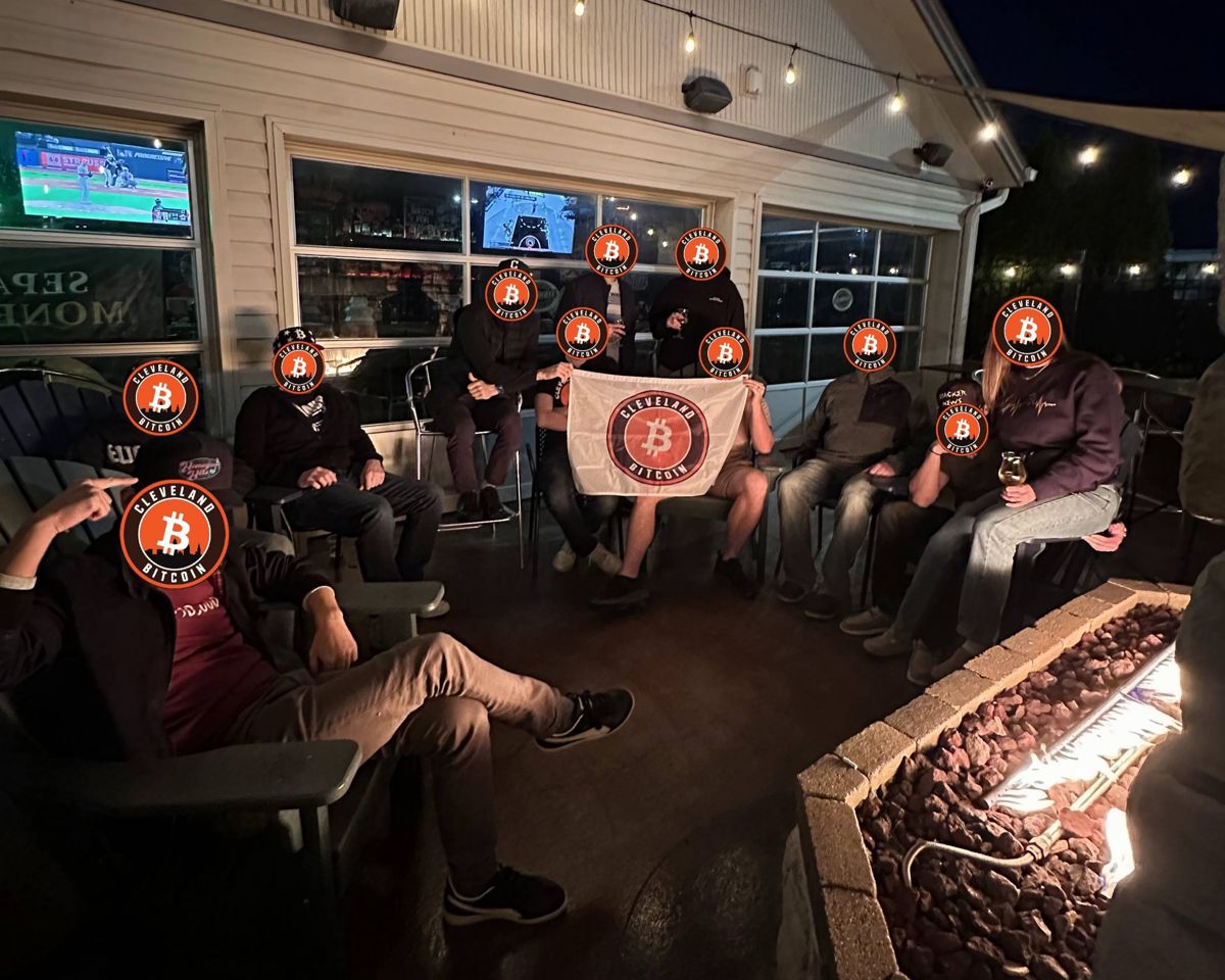 The Cleveland Bitcoin meetup on a patio around a fire pit, holding a Cleveland Bitcoin flag. Every face is covered with the meetup's logo.